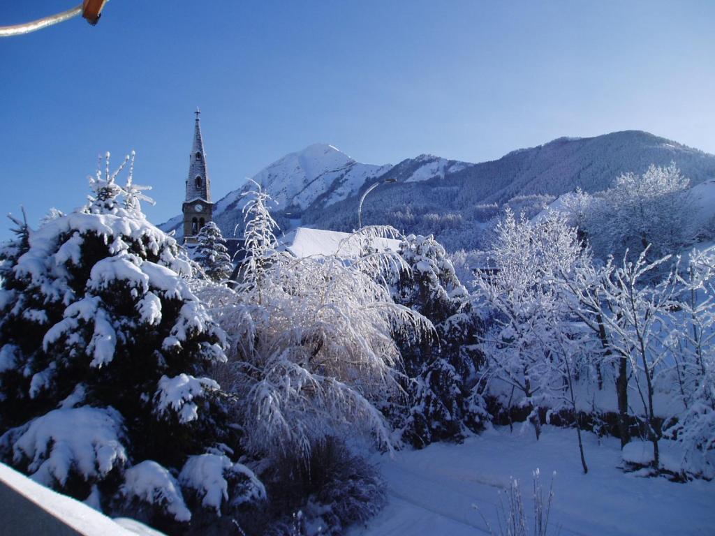 un groupe d'arbres recouvert de neige avec une église dans l'établissement Les Garianes, à Saint-Léger-les-Mélèzes