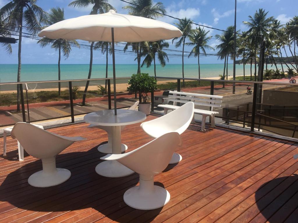 un patio con sillas blancas y una sombrilla y la playa en Frente Mar - Duas Suítes no C.Branco, en João Pessoa
