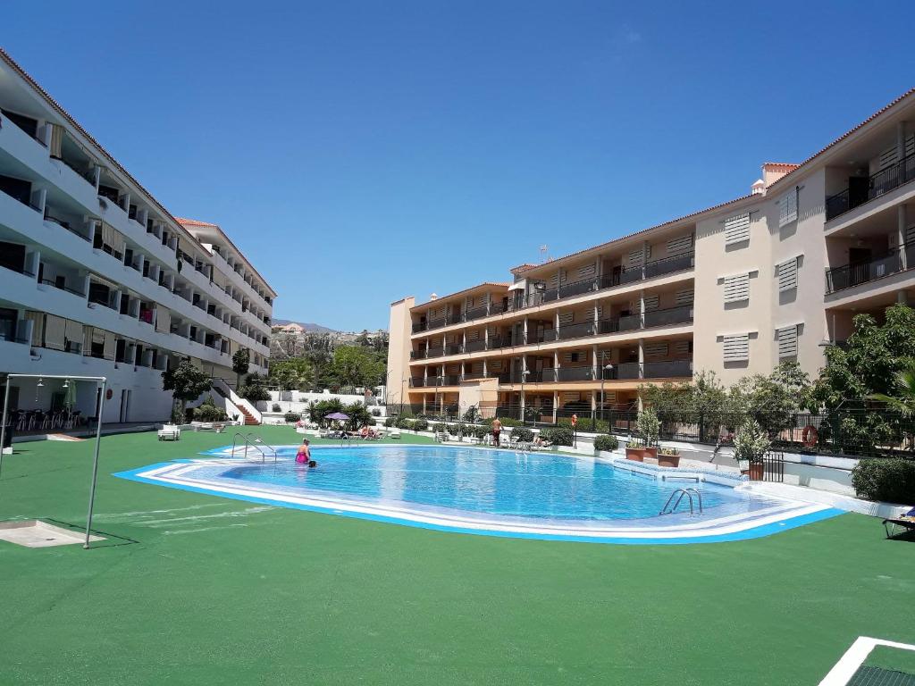 een groot zwembad met een groen gazon voor de gebouwen bij Summerland LC Holiday Home in Los Cristianos