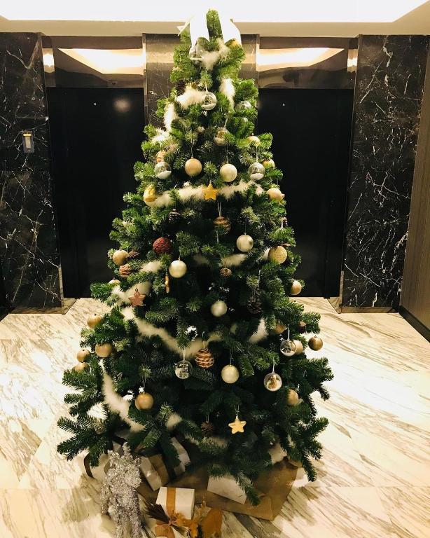 A decorated Christmas tree with wrapped presents in a marble-floored elevator lobby.