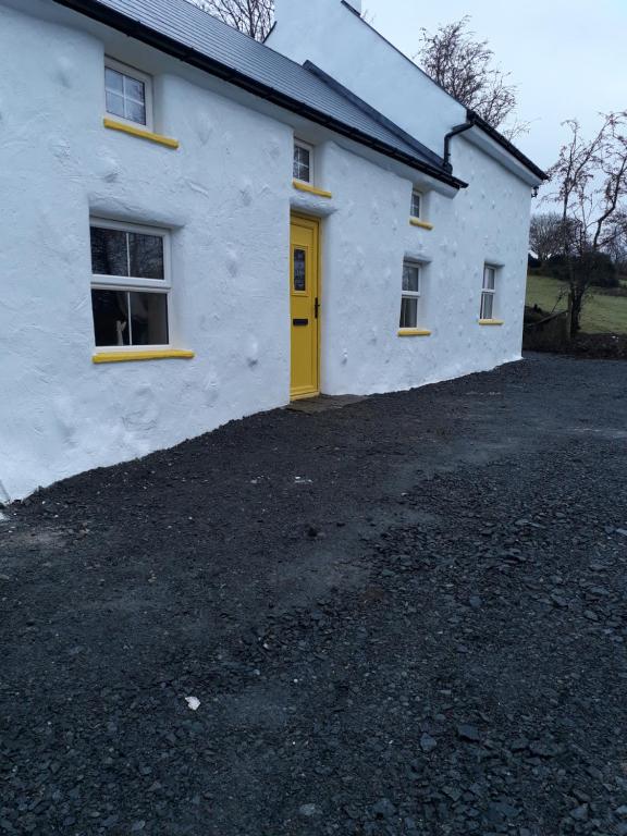 a white house with a yellow door and a driveway at Sams cottage in Corderry