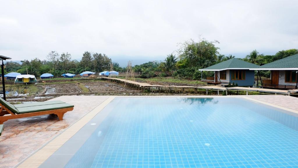 una piscina junto a una casa con sombrillas en Nok Chan Mee Na en Chom Thong