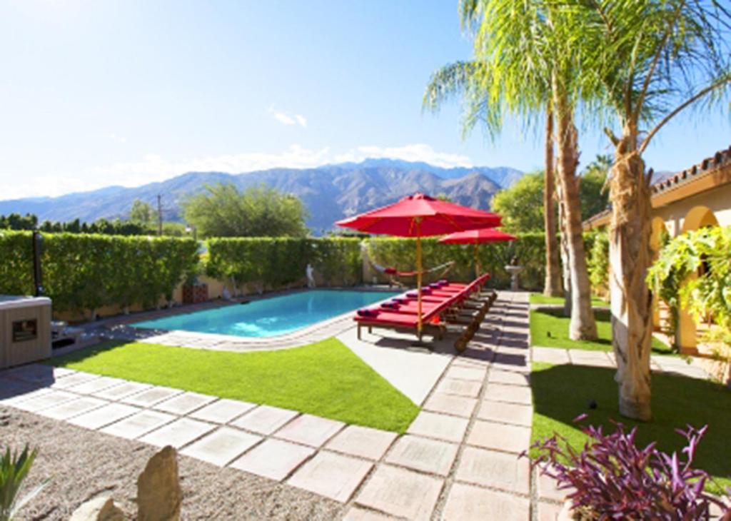 a pool with two benches and a red umbrella at Villa Cristine - Spanish Style Palm Springs Villa in Palm Springs