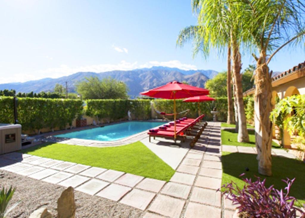 a pool with two benches and a red umbrella at Villa Cristine - Spanish Style Palm Springs Villa in Palm Springs