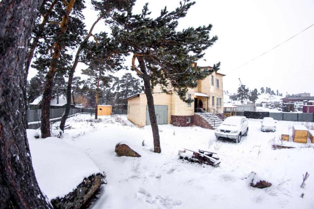 a snow covered yard with a house and cars at Guest House Palletto_borovoe in Borovoye