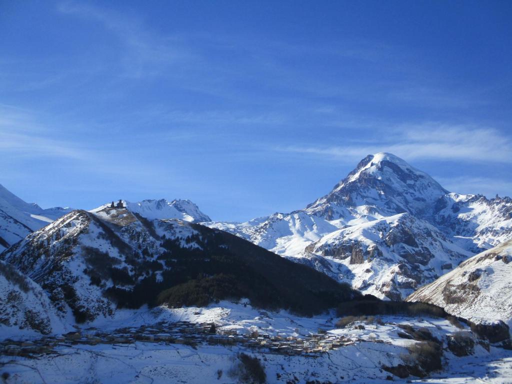 einen schneebedeckten Berg mit einer Stadt davor in der Unterkunft The White House in Kazbegi