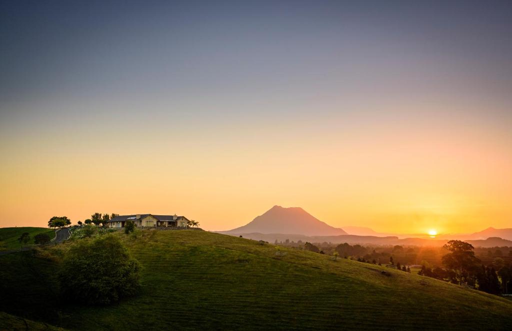 a house on a hill with the sunset in the background at Secret Lake Farmstay in Whakatane