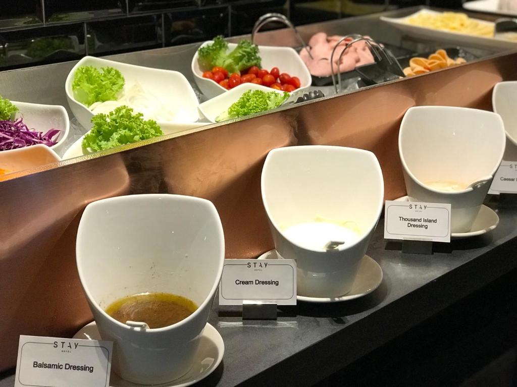 A buffet counter with salad vegetables and individually labelled dressing bowls.