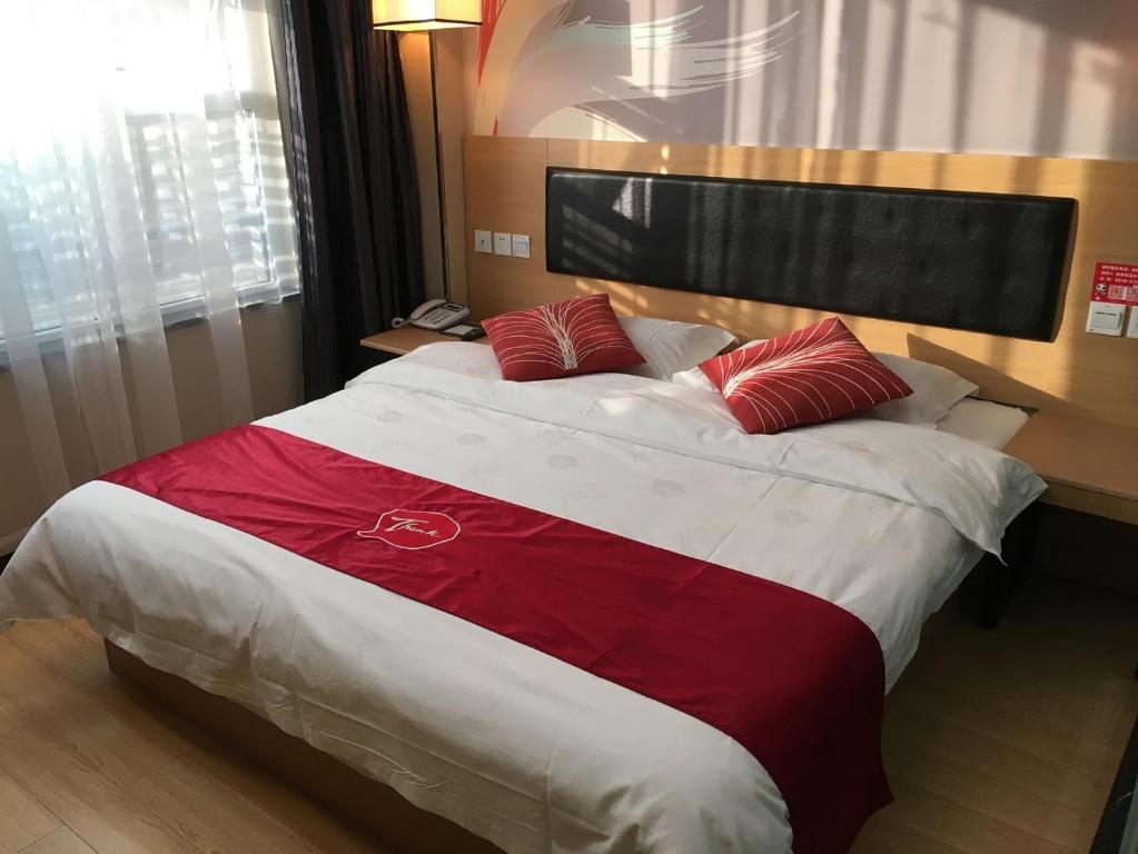 uma cama grande com lençóis vermelhos e brancos e almofadas vermelhas em Thank Inn Chain Hotel Sichuan Dazhou Tongchuan Dis. Railway Station em Dazhou