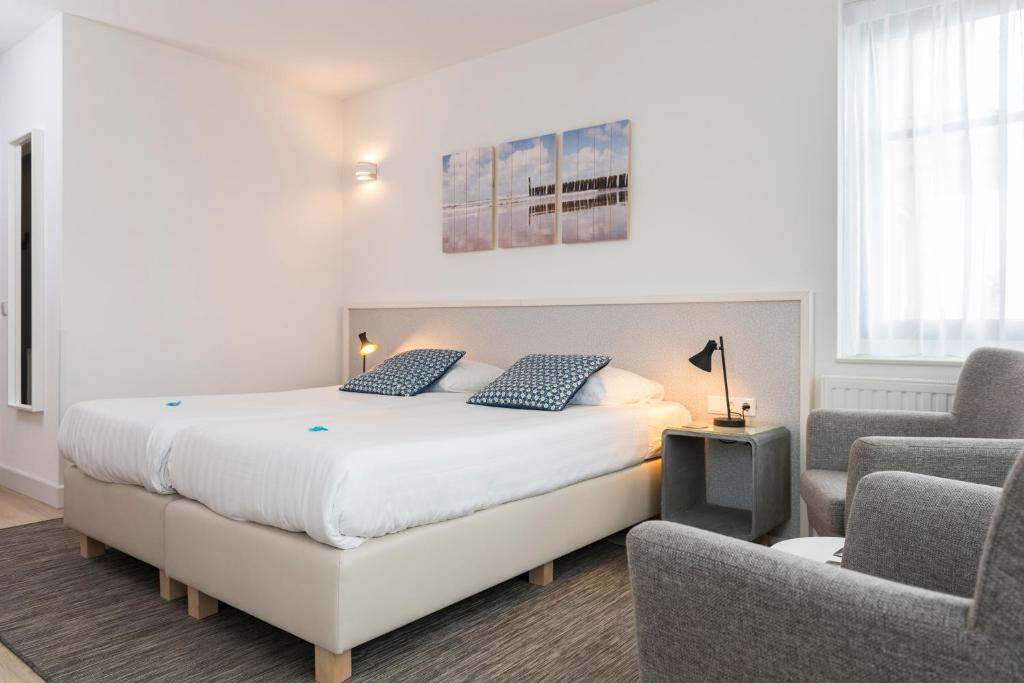 a white bedroom with a bed and a chair at Hotel Bosch En Zee in Domburg