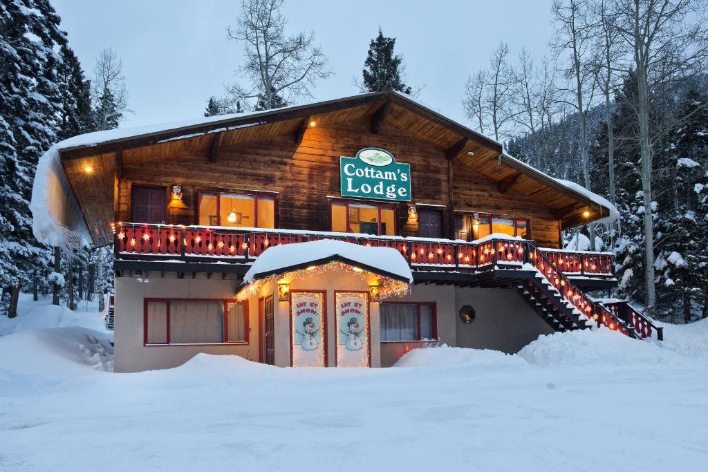 a log cabin with christmas lights in the snow at Cottam's Lodge by Alpine Village Suites in Taos Ski Valley