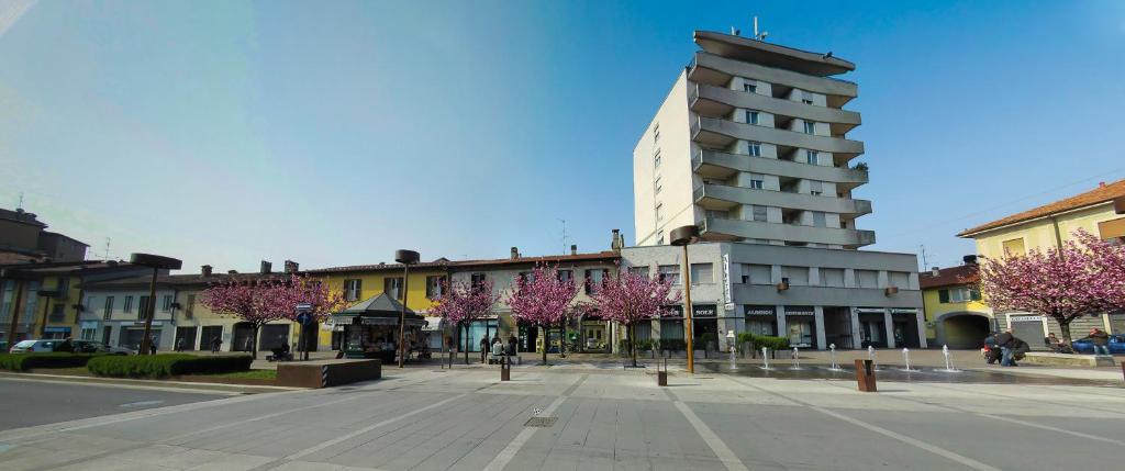 eine Stadtstraße mit einem Gebäude und Bäumen mit rosa Blumen in der Unterkunft Albergo Sole in Mariano Comense