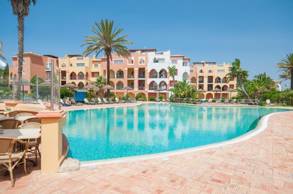 a swimming pool in a resort with palm trees and buildings at Jardim da Meia Praia Resort in Lagos