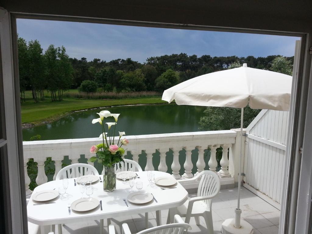 d'une table blanche avec des chaises et un parasol sur le balcon. dans l'établissement Port Bourgenay Ile au Pré vue lac et golf, à Talmont-Saint-Hilaire