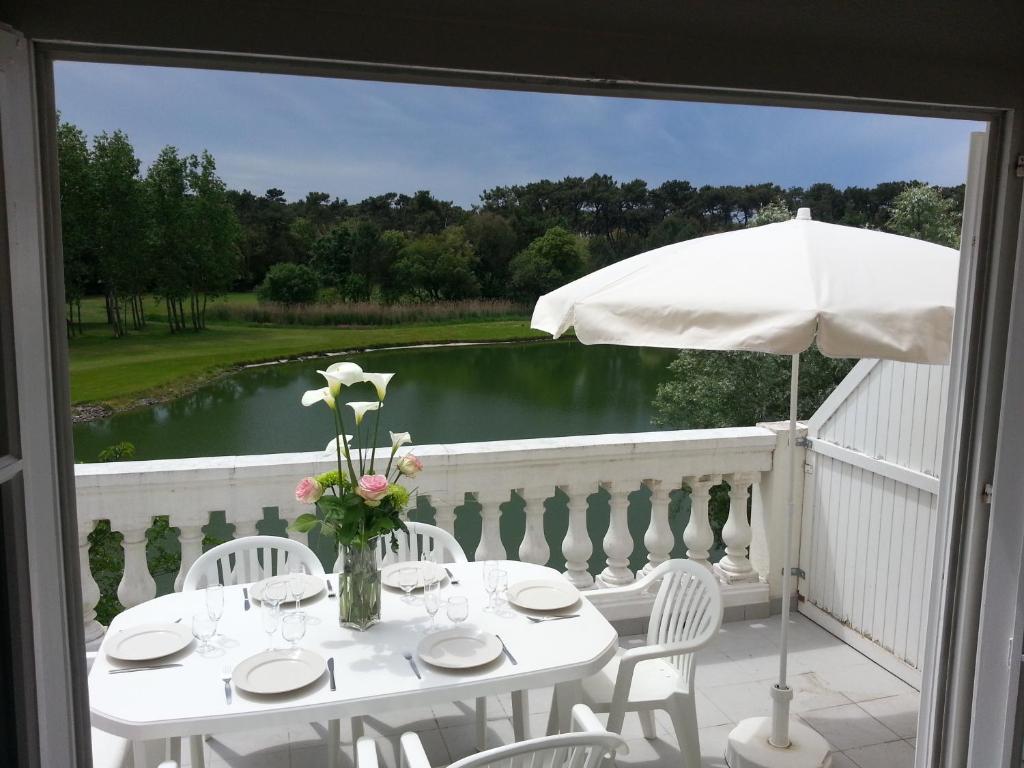 d'une table blanche avec des chaises et un parasol sur le balcon. dans l'établissement Ile au Pré vue lac et golf, à Talmont-Saint-Hilaire