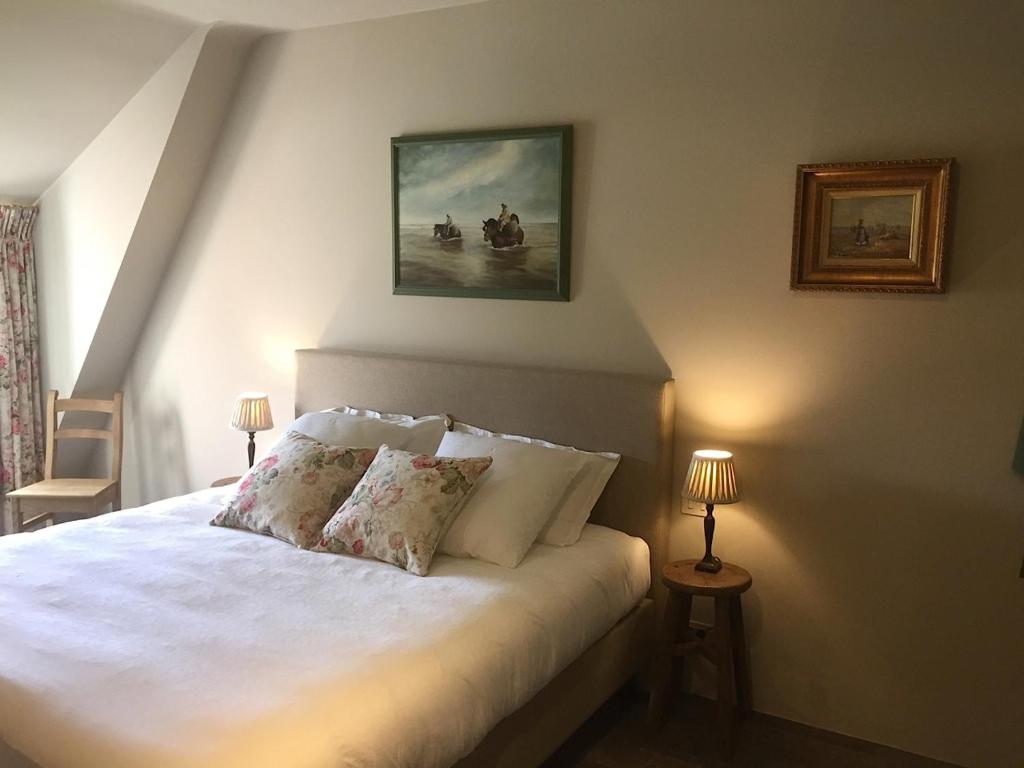 een slaapkamer met een wit bed met kussens en een schilderij bij de Gasterie in Koksijde