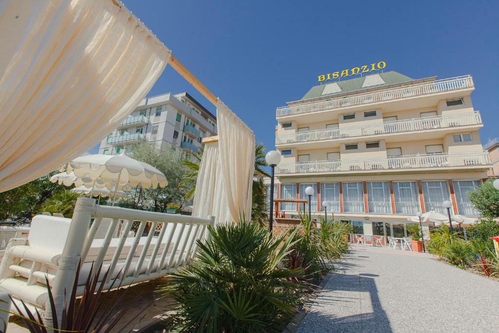 ein Hotel mit Stühlen, einem Regenschirm und einem Gebäude in der Unterkunft Hotel Bisanzio in Cesenatico