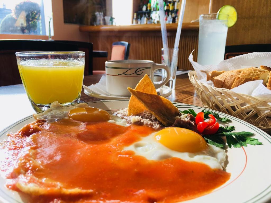 A full breakfast plate of eggs in red sauce served with juice, coffee, bread, and a citrus drink.