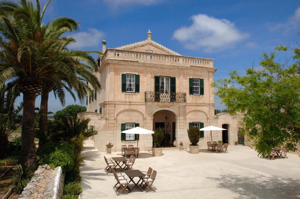 ein Gebäude mit Stühlen und Sonnenschirmen davor in der Unterkunft Alcaufar Vell Hotel Rural & Restaurant in Sant Lluís