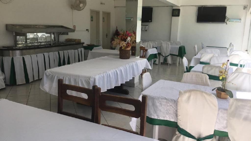 Una habitación con mesas y sillas blancas con flores. en Hotel Kika, en São Gabriel