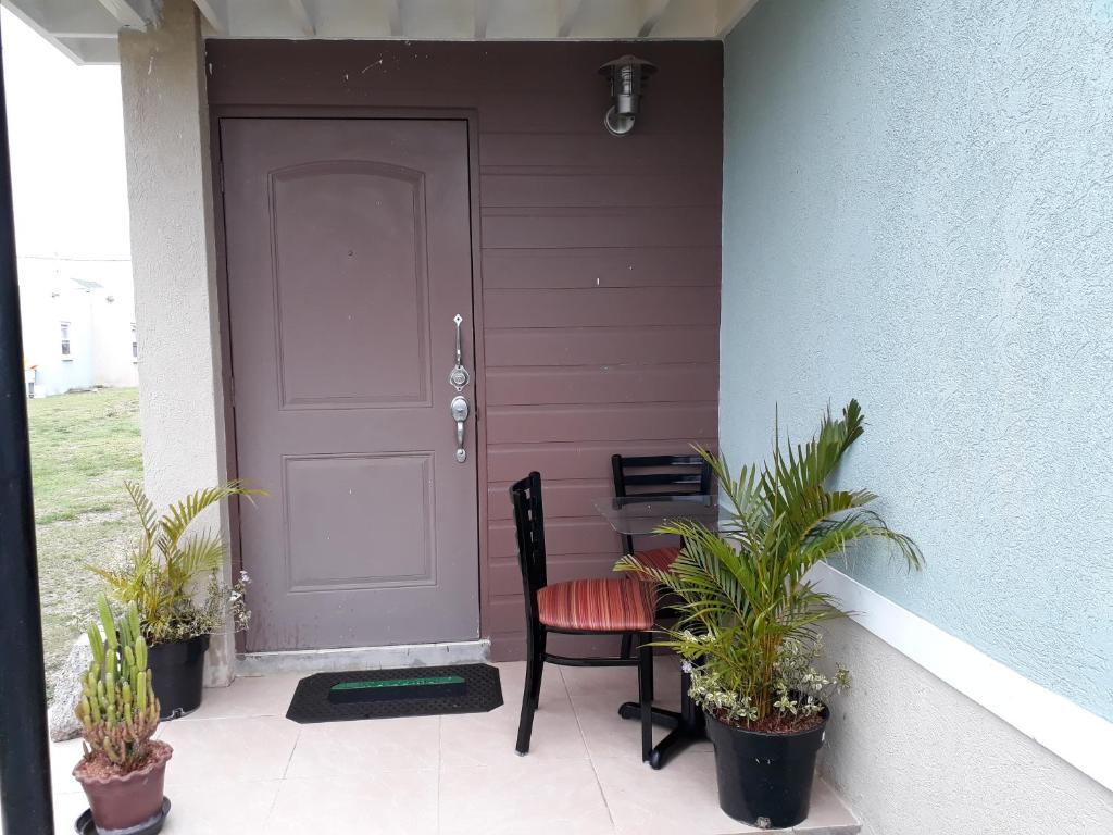 a porch with a purple door and a chair and plants at Jacaranda Homes in Spanish Town