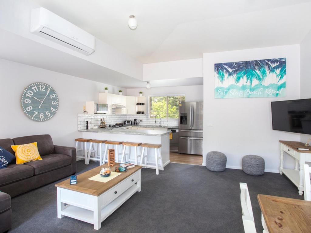 a living room with a couch and a kitchen at Fairway Haven Getaway in Mollymook