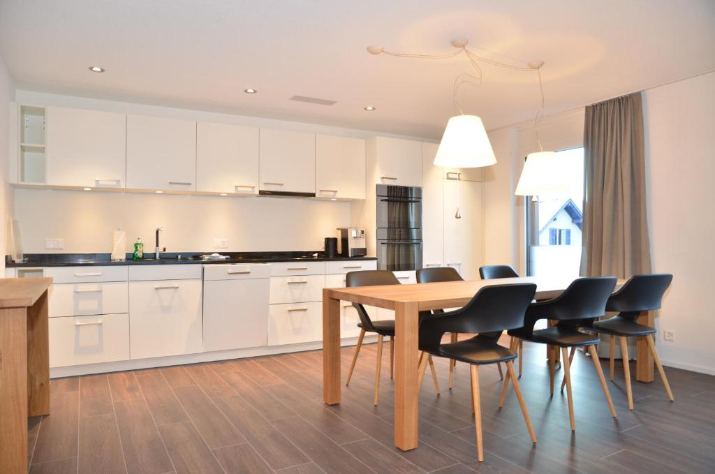 Apartment Narzisse - GriwaRent AG في إنترلاكن: مطبخ بدولاب بيضاء وطاولة وكراسي خشبية