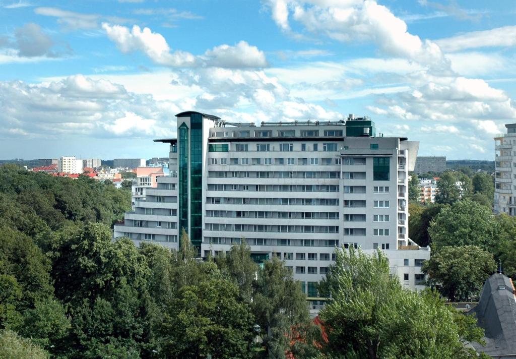 a large white building with trees in front of it at Etna Polonia Apartamenty in Kołobrzeg