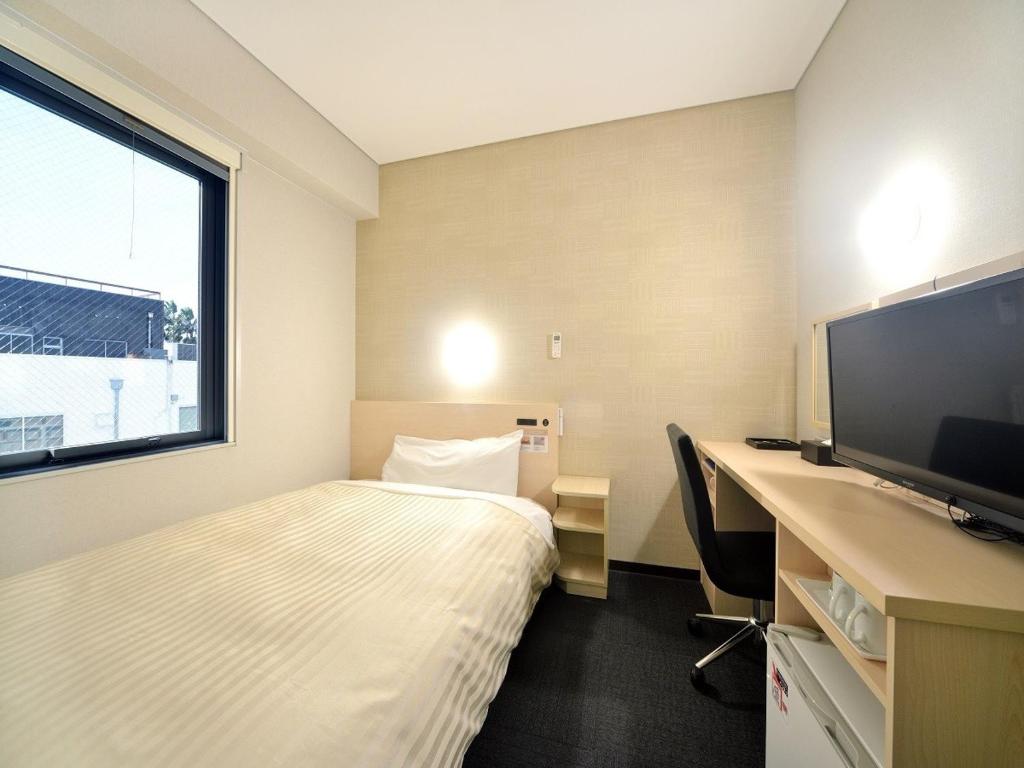 um quarto de hotel com uma cama e uma secretária com uma televisão em Super Hotel Miyazaki Natural Hot Springs em Miyazaki
