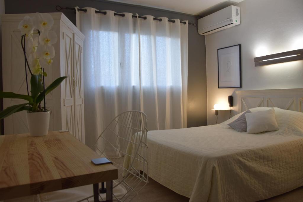 a bedroom with a bed and a table and a window at Hôtel le Grillon in LʼÎle-Rousse