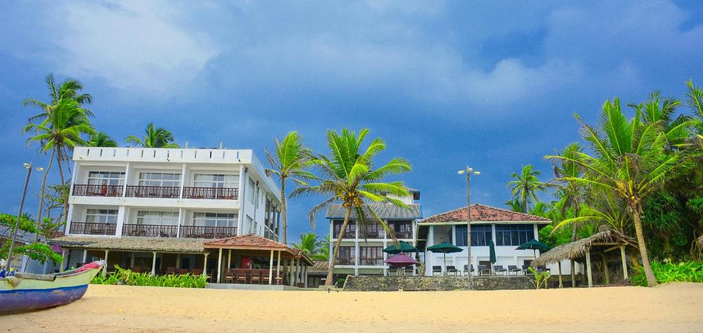 a building on a beach with palm trees and a boat at Ranmal Beach Hotel in Hikkaduwa