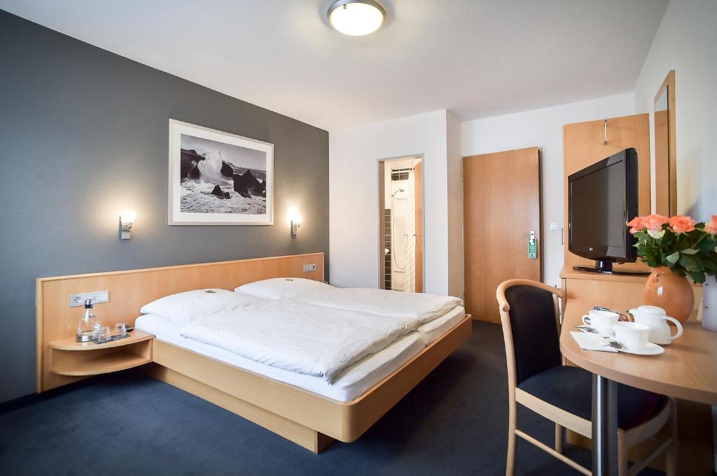 a bedroom with a bed and a desk and a tv at Hotel Mautner Airport und Messehotel in Stuttgart