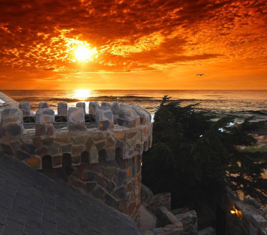 a sunset over the ocean with a stone wall at Hotel Boutique Castillo del Mar in El Quisco