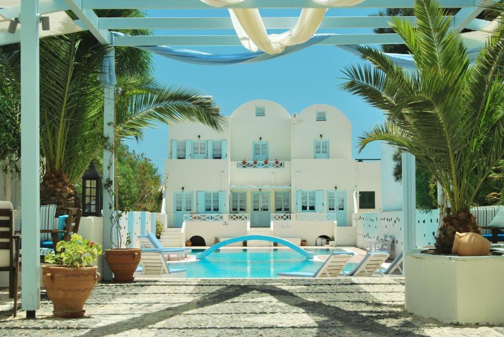 a pool in the middle of a resort with palm trees at Aeolis Santorini in Perissa