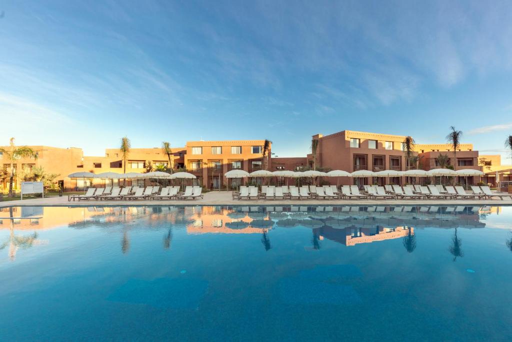 une grande piscine d'eau avec des chaises et des bâtiments dans l'établissement Be Live Experience Marrakech Palmeraie - All Inclusive, à Marrakech