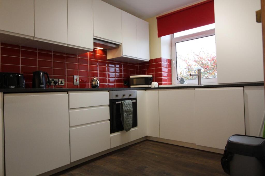 uma cozinha com armários brancos e uma parede de azulejos vermelhos em Townlets Serviced Accommodation Salisbury em Belfast