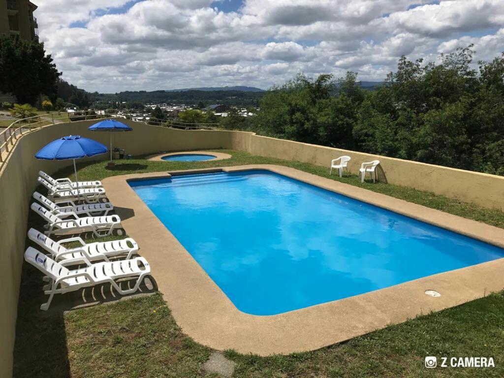una piscina con tumbonas y sombrilla en Villarrica Mirador Apartment, en Villarrica