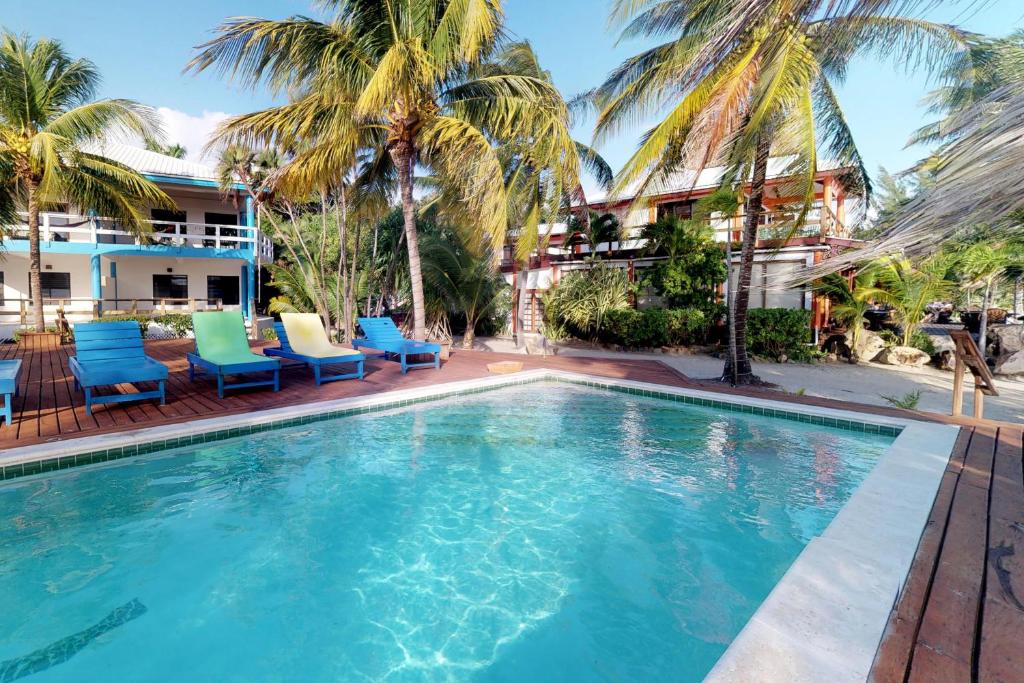 una piscina con palmeras y sillas azules y verdes en Condo #31 @ Beachside Villas en Placencia Village