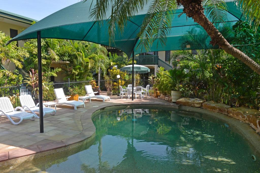 a pool with an umbrella and chairs and a patio at City Gardens Apartments in Darwin