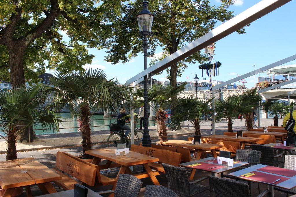 een restaurant met houten tafels en stoelen en bomen bij East West Hotel Basel in Bazel