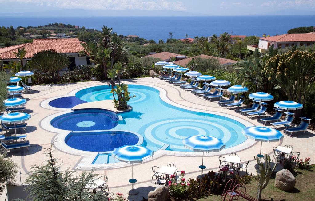 a pool with blue umbrellas and chairs and the ocean at Il Gattopardo in Capo Vaticano