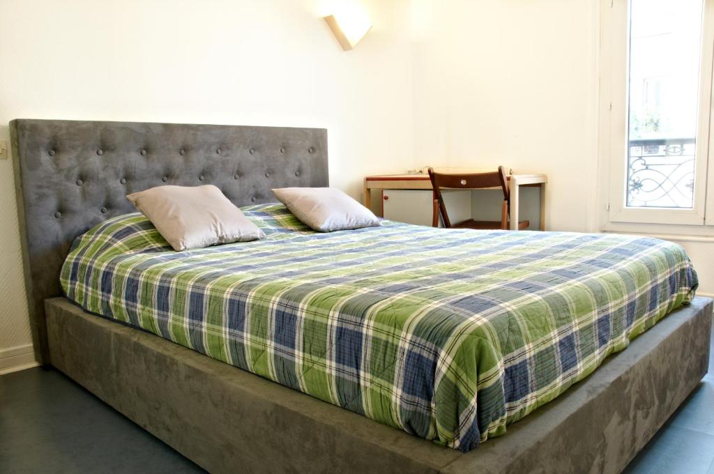a bed with a blue and green plaid blanket at Hotel Luxor in Issy-les-Moulineaux