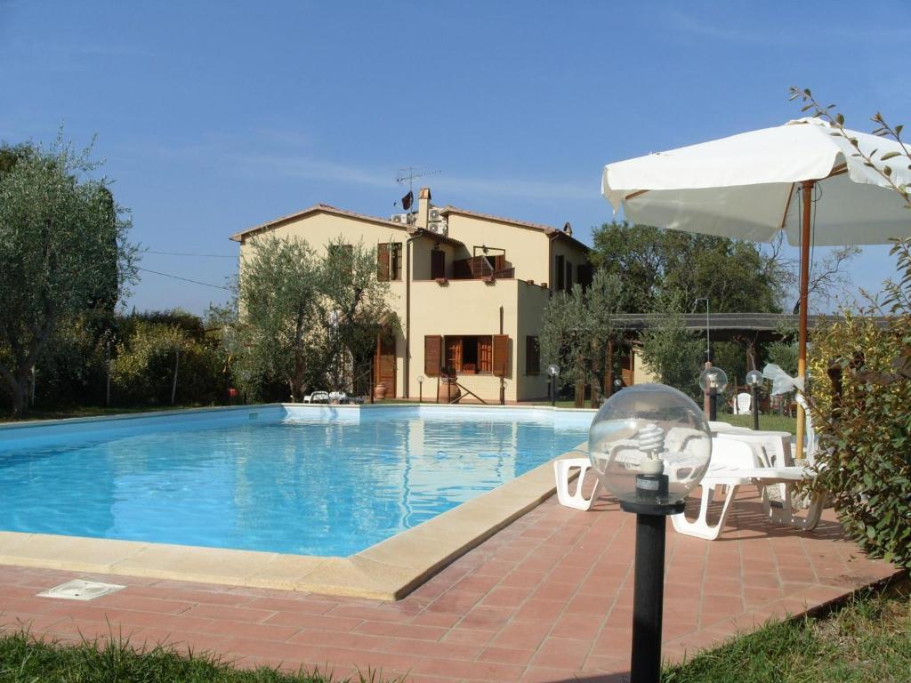 a swimming pool in front of a house with an umbrella at Podere Cortesi Agriturismo Molinaccio in Santa Luce