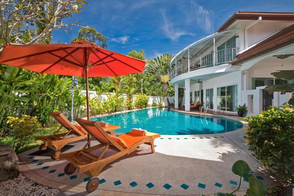 einen Pool mit 2 Stühlen und einem roten Regenschirm in der Unterkunft Villa Sirion in Kamala Beach