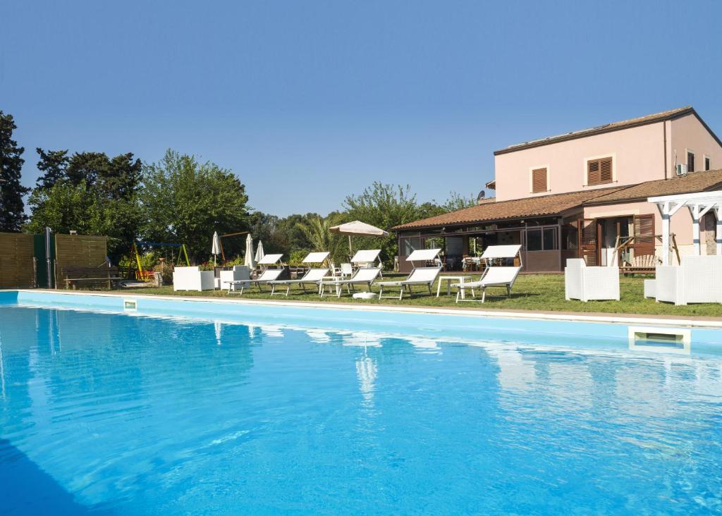 une grande piscine avec des chaises et une maison dans l'établissement Sicily Country House & Beach, à Catane