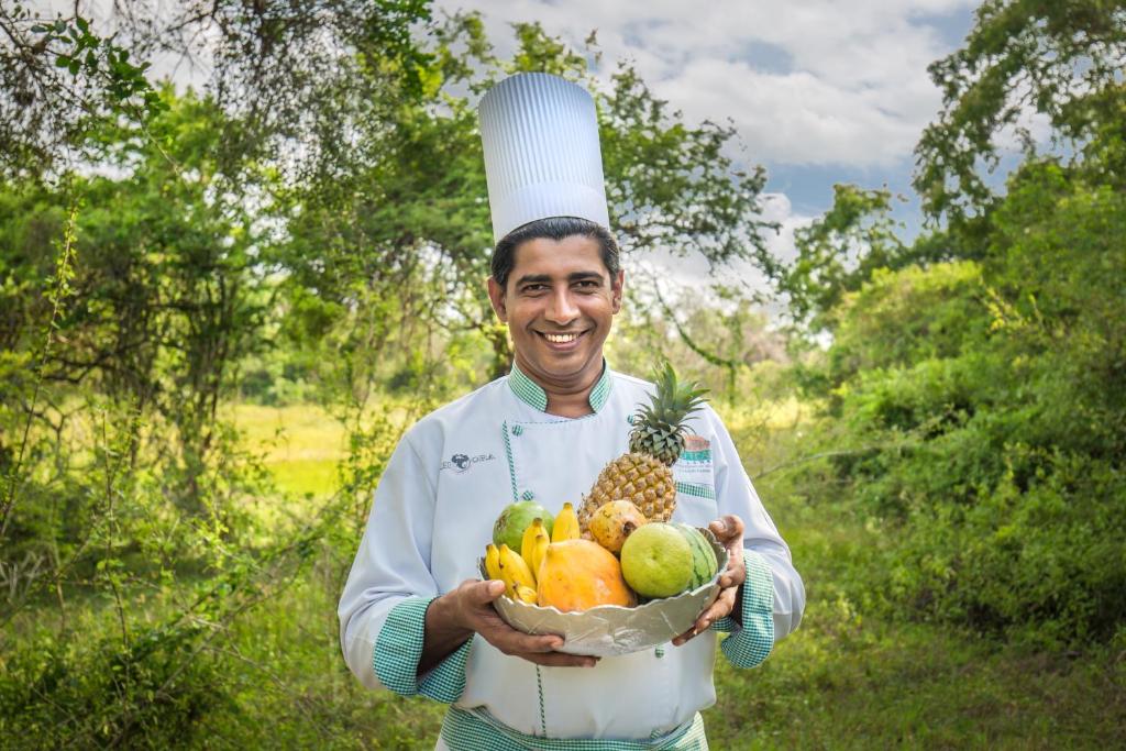 a man wearing a chefs hat holding a bowl of fruit at Mahoora Wilpattu - by Eco Team in Wilpattu