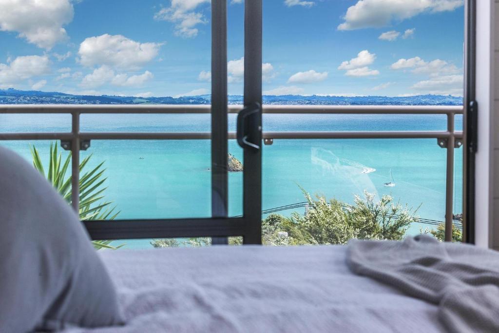 a room with a view of the ocean from a bed at Sunset Sanctuary- Waiheke Escapes in Omiha
