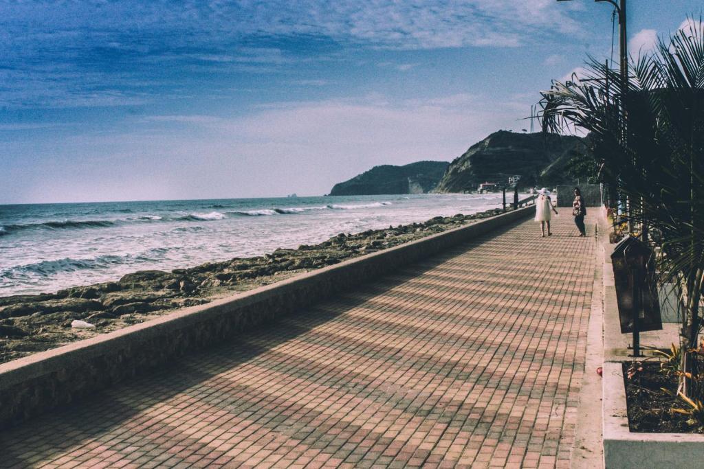 dos personas caminando por una acera junto a la playa en Hotel Estación del Sol, en Las Núñez