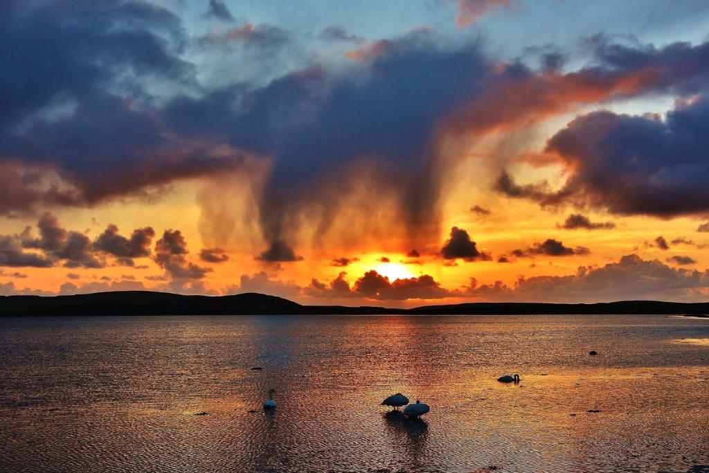 um pôr do sol sobre um grande corpo de água com nuvens em Nether Onston Cottage em Stenness