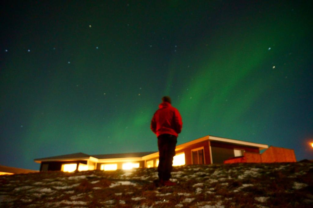 una persona de pie en una colina mirando la aurora boreal en Guesthouse 46, en Hvammstangi
